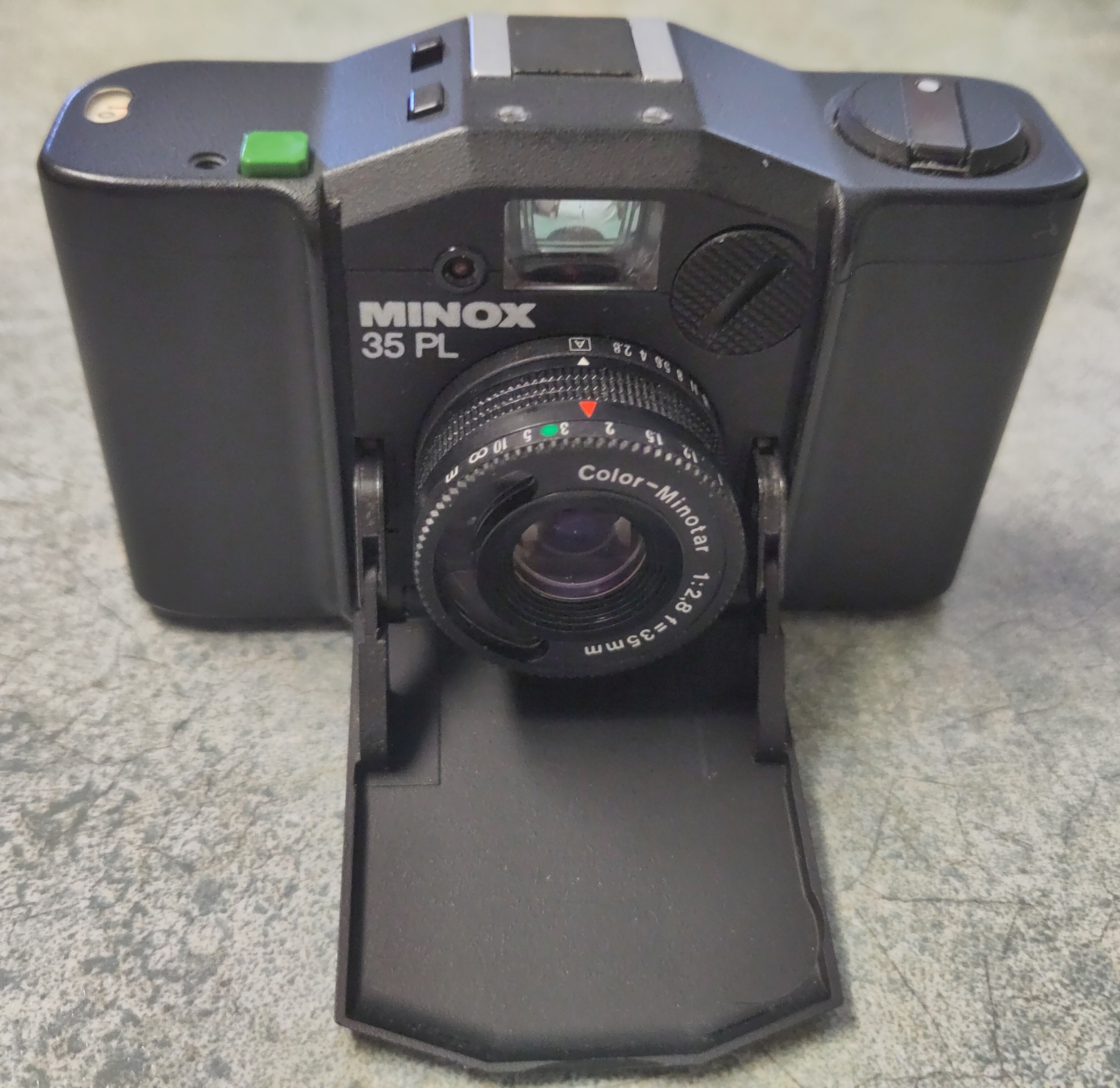 Minox 35 PL - die kleine schwarze Analogkamera ist von vorn mit geöffneter Klappe fotografiert.